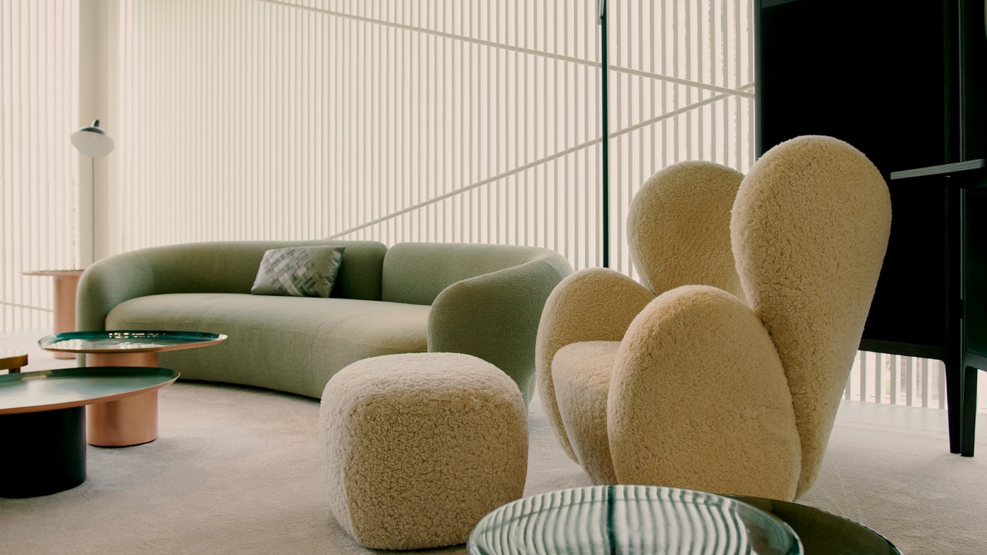Plano médio: sofá curvo verde ao lado de poltronas e pufe em pelo natural